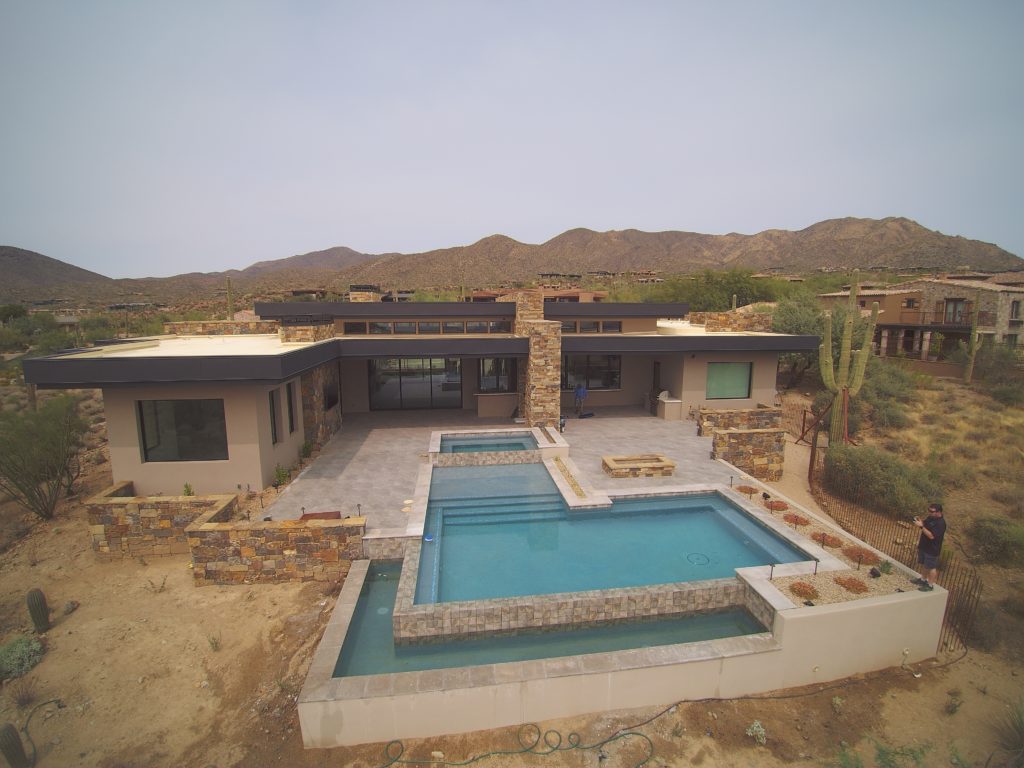 An Arizona home with mountains in the background and a two tier l shaped swimming pool.