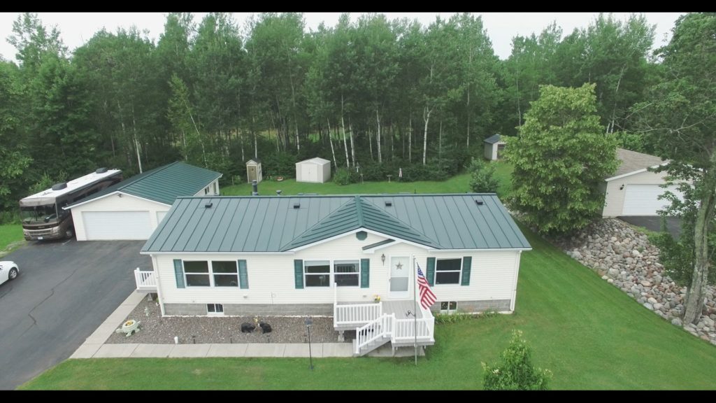 A green metal roof on a white house in the country.