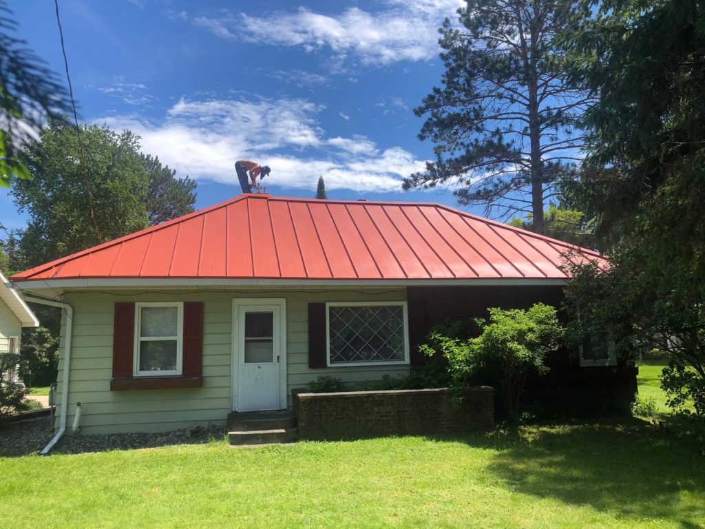 A Vertex Roofing crew member installing a new red standing seam metal roof on a home.