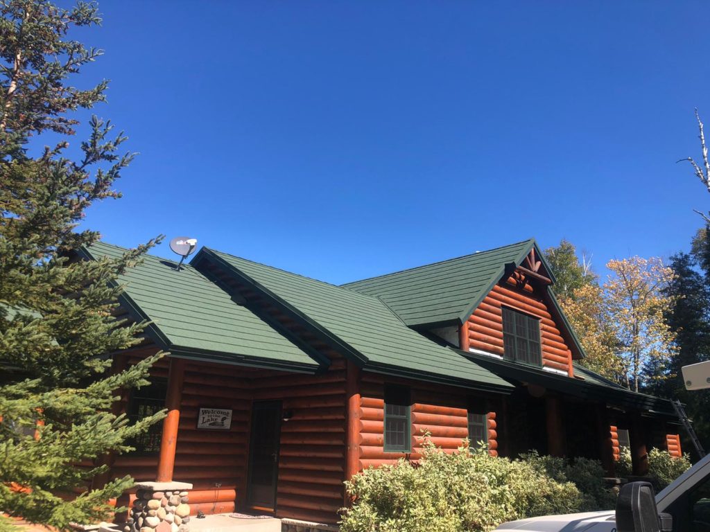 A red log cabin type home with a new green stone coated steel roof installed by Vertex Metal Roofing.