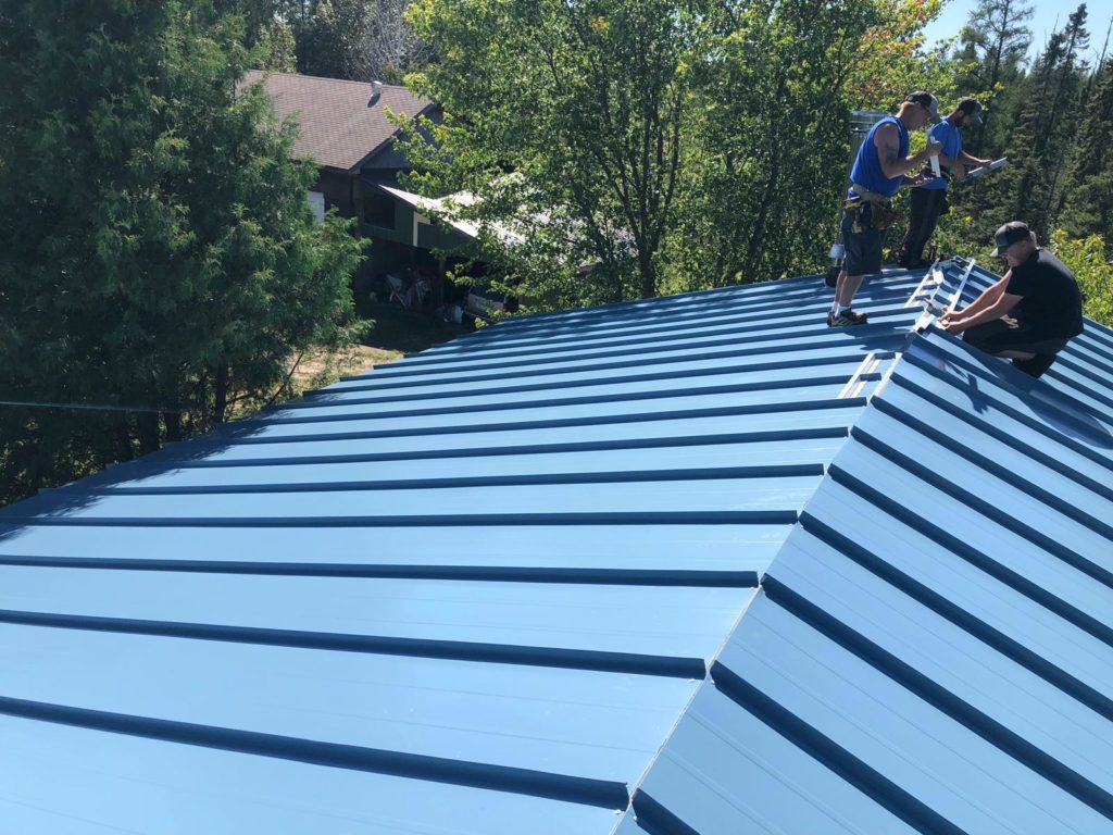 roofers installing a blue metal roof.