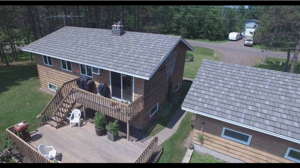 A drone view of a home with a new gray metal shake roof on the home and a detached building.