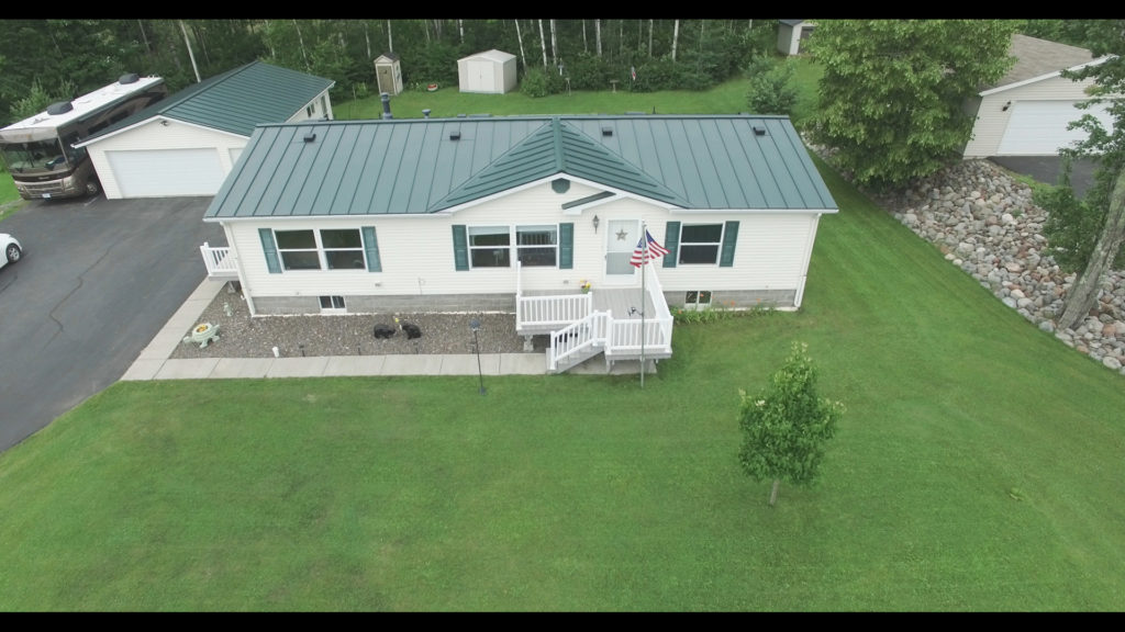 Overhead view of a white home with a lush yard and green standing seam metal roofing installed on the home and a detached garage.