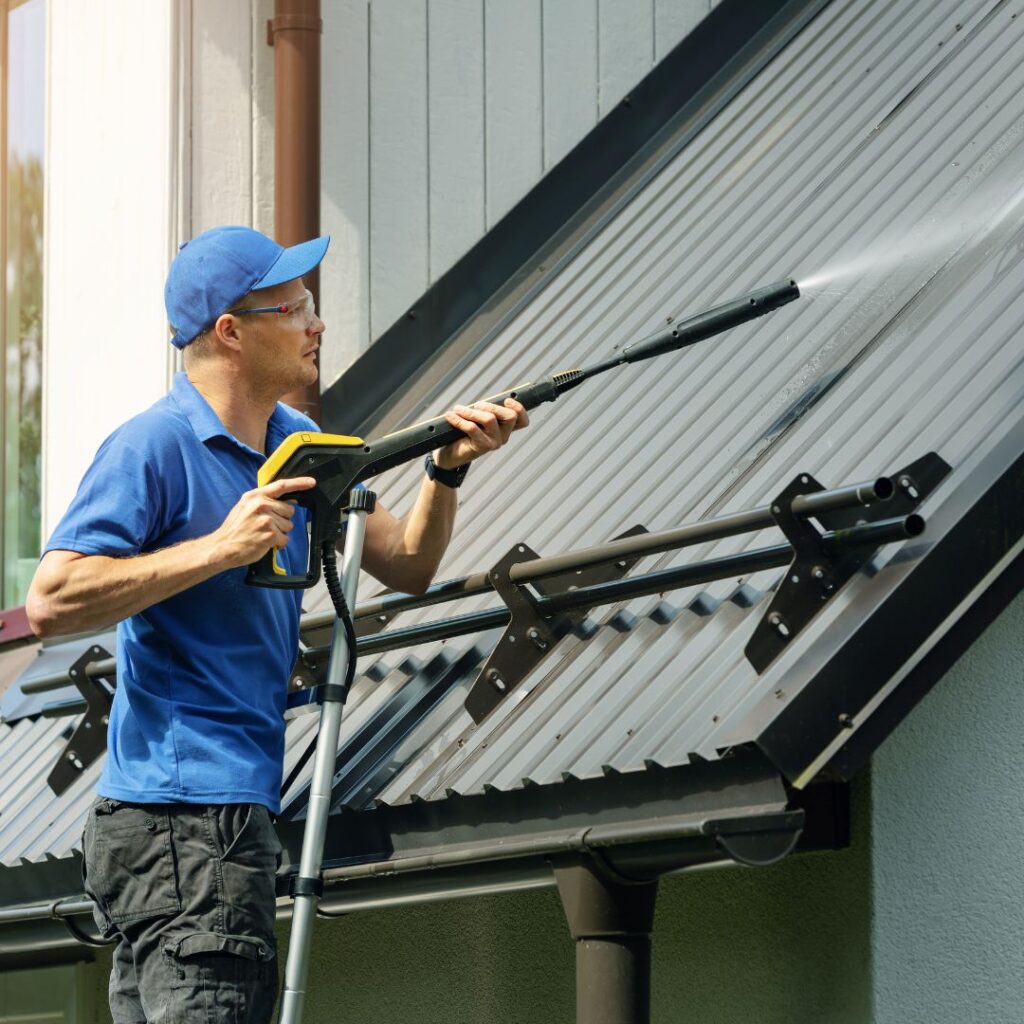 Man pressure washing a metal roof